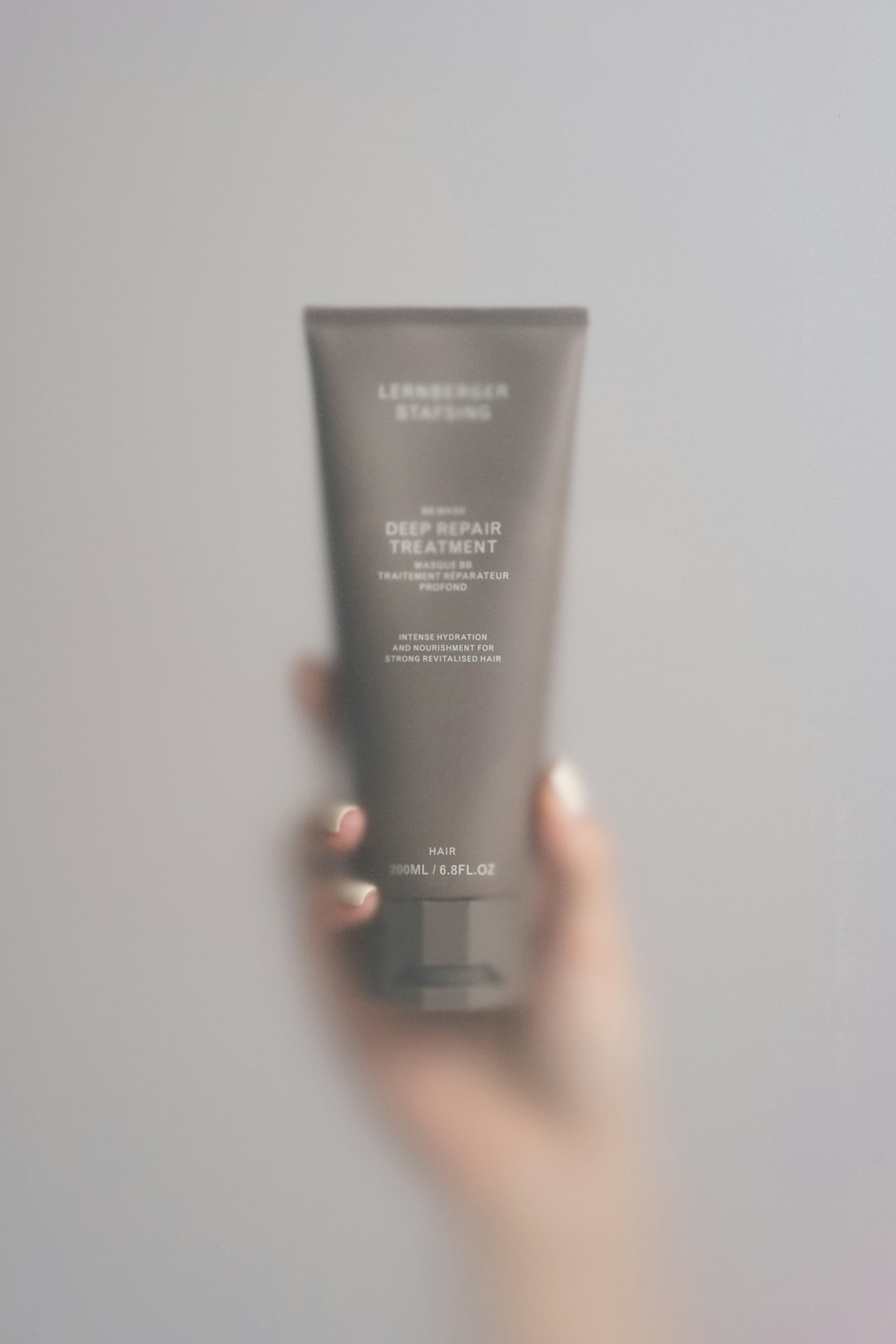 about-us A sleek, matte taupe tube labeled as a deep repair treatment for hair. The minimalistic design features white text detailing intense hydration and nourishment. The soft focus and gentle lighting create an elegant, airy feel.