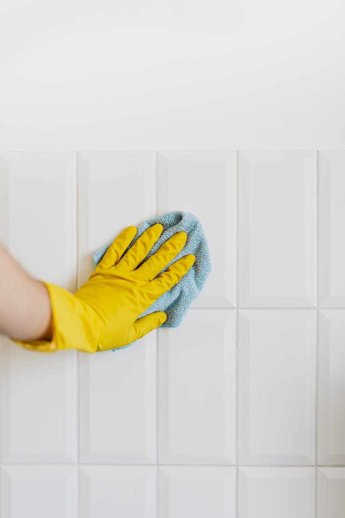 who-we-are Crop unrecognizable person in yellow rubber gloves cleaning white tile wall with blue microfiber cloth in daylight